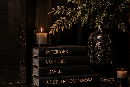A candle, a dark marbled vase, and a stack of books titled Interiors, Culture, Travel, and A Better Tomorrow
